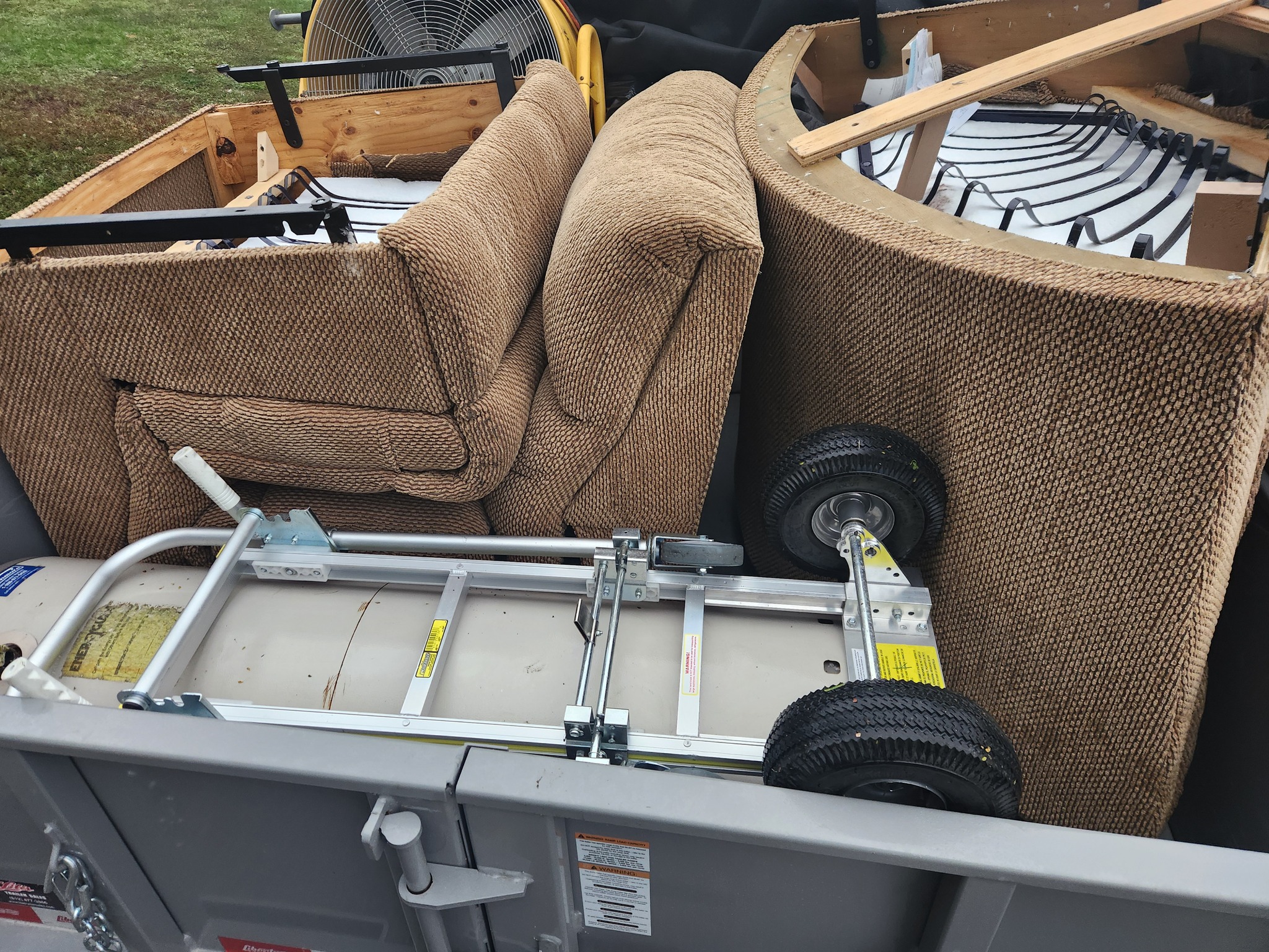 Dump trailer filled with broken furniture pieces, cushions, and equipment from a residential junk removal job.