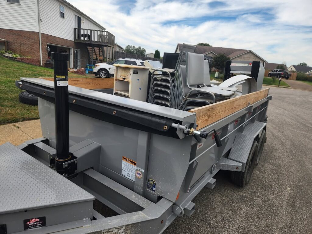 Dump trailer filled with stacked metal chairs, household items, and debris during a residential cleanout.