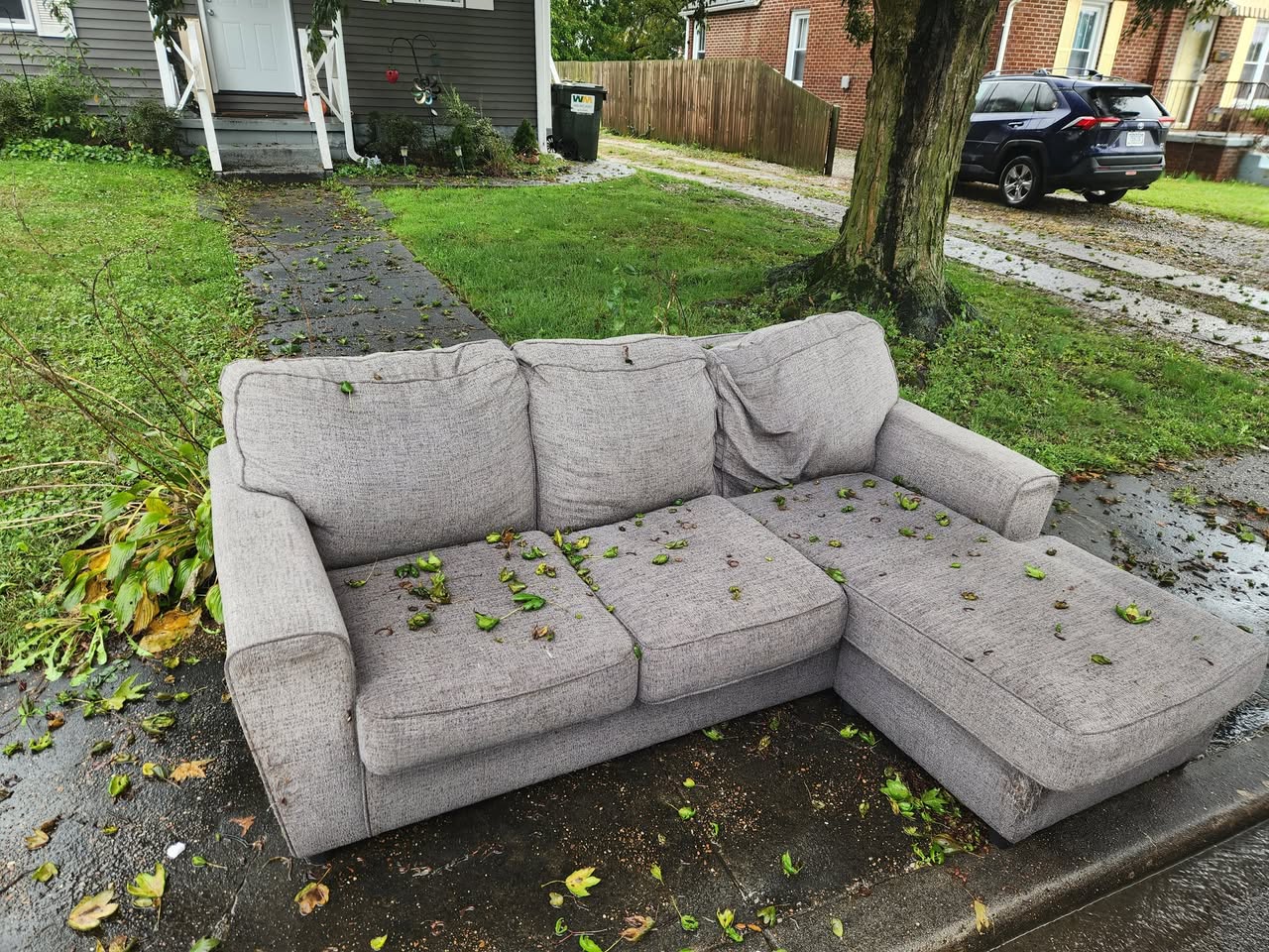 Gray sectional couch left at the curb for bulk item pickup after a residential furniture removal.
