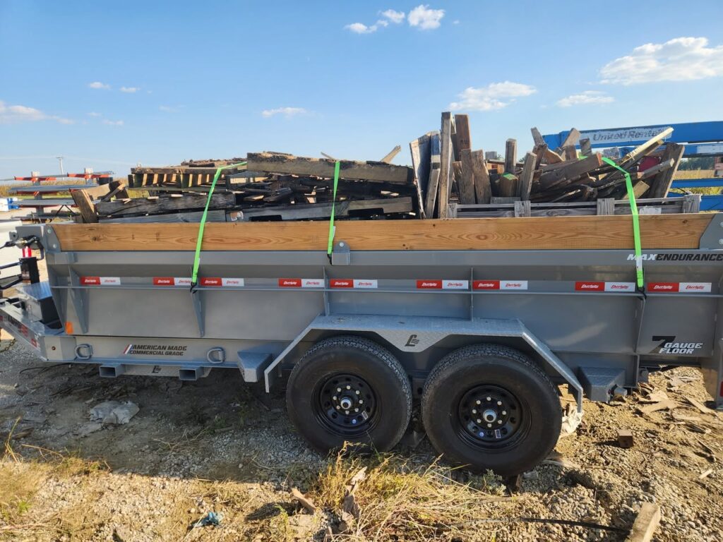 Dump trailer carrying broken wooden pallets secured with green straps during a debris removal job.