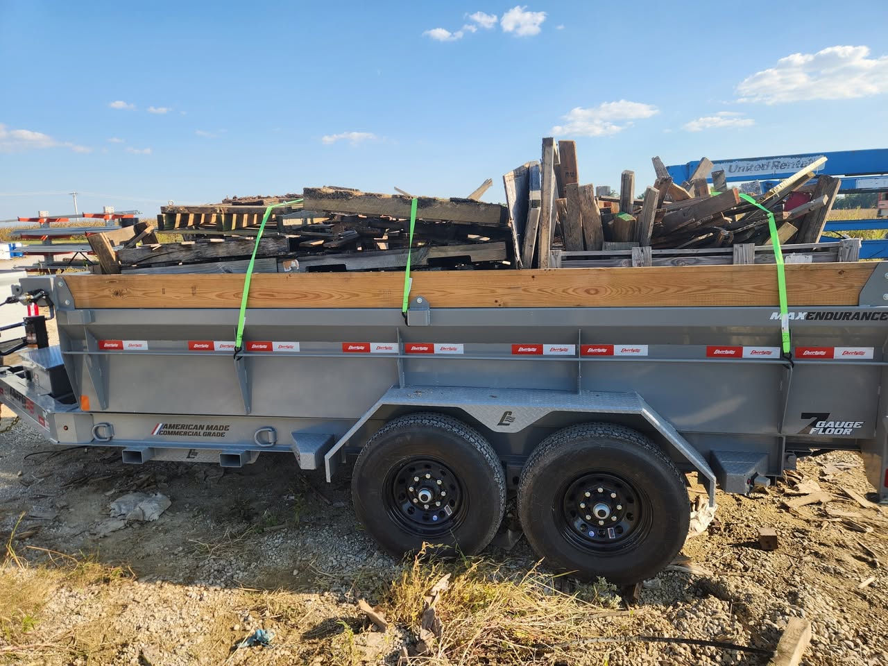 Dump trailer carrying broken wooden pallets secured with green straps during a debris removal job.